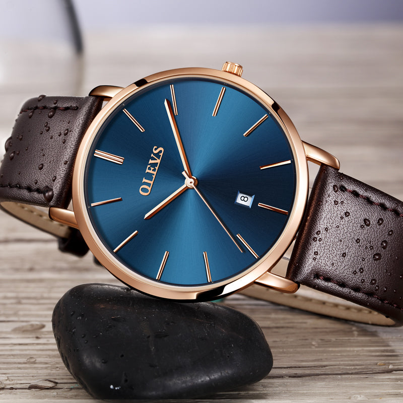 Men's OLEVS watch with blue dial, gold case, and brown leather strap on wooden surface