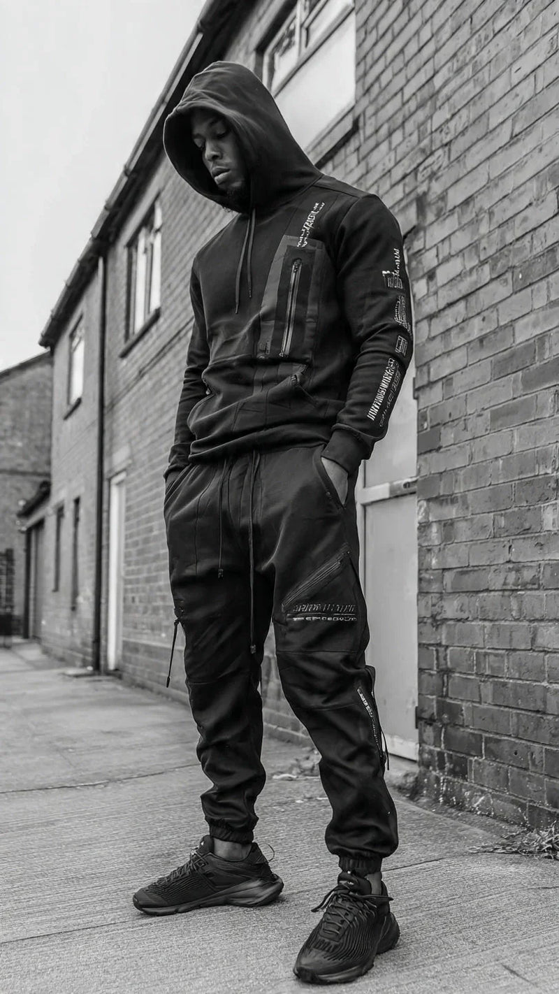 Man in black two-piece tracksuit with hoodie and sneakers, urban street style, FashionRay