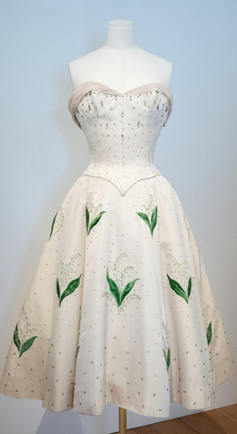 Elegant strapless cream floral dress with green leaf designs, showcased on a mannequin at FashionRay.