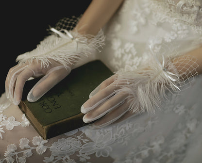 Woman in white lace dress with feathered mesh gloves holding book, elegant fashion detail