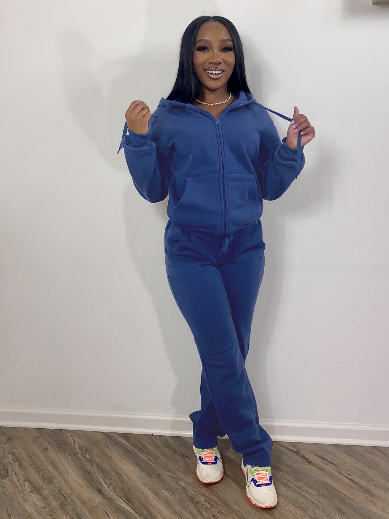 Woman wearing a royal blue tracksuit and colorful sneakers, smiling indoors on wood floor