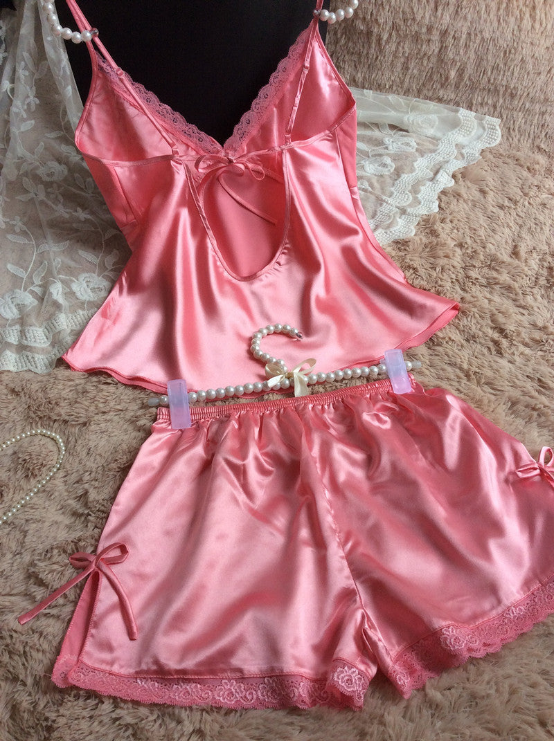 Pink satin lace camisole and shorts sleepwear set on a textured beige surface