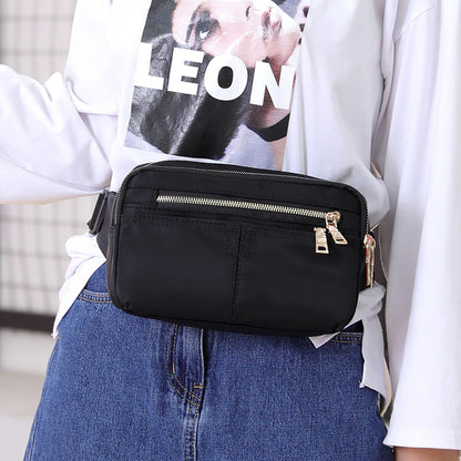 Black waist bag with gold zippers styled over jeans and white graphic shirt, FashionRay