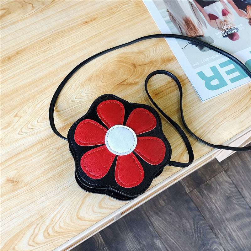 FashionRay black flower-shaped crossbody bag with red petals on a wooden table