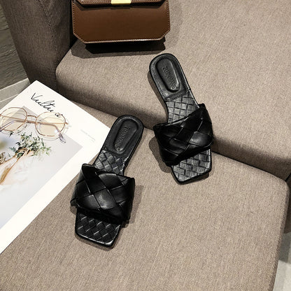 Black woven slides on beige sofa, next to brown purse and magazine, FashionRay style