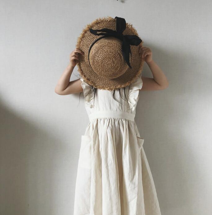 Girl in white dress holding straw hat with black ribbon, FashionRay trendy kids fashion