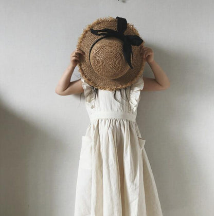 Girl in white dress holding straw hat with black ribbon, FashionRay trendy kids fashion