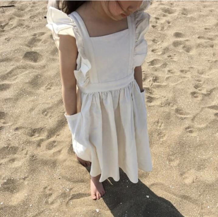 Girl in a white ruffle sundress standing on sandy beach, FashionRay trendy kidswear