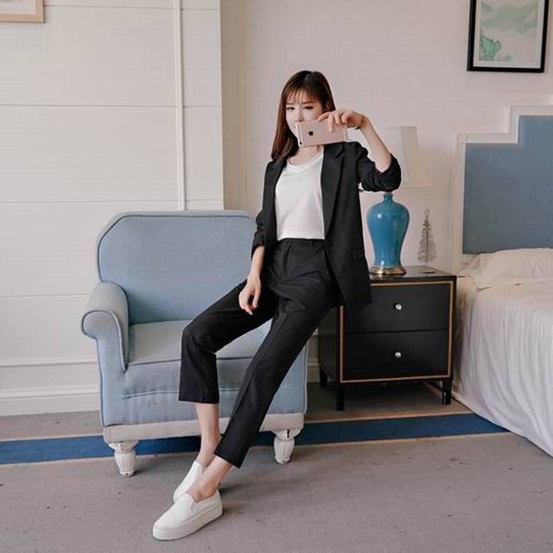 Woman in black suit and white sneakers taking selfie, FashionRay modern trendy outfit.