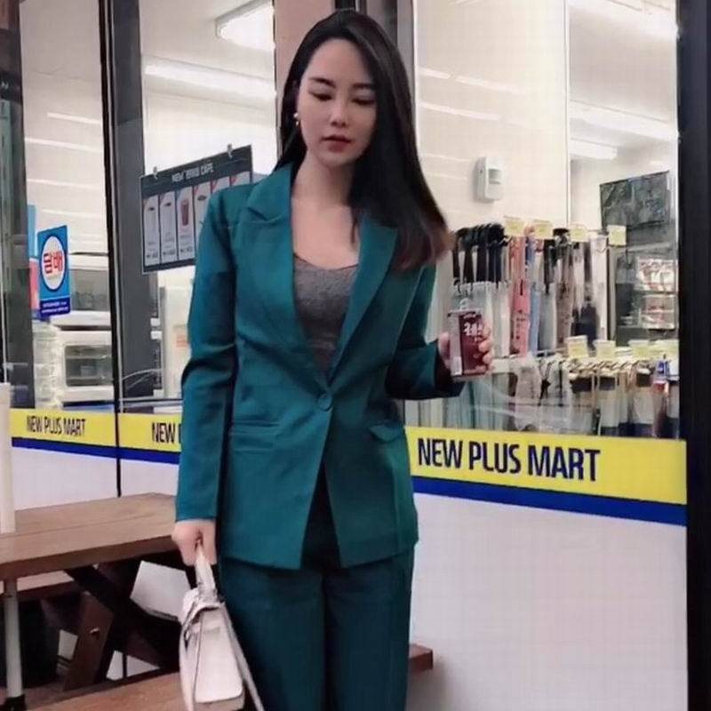 Woman in teal suit holding drink and white handbag outside convenience store, stylish FashionRay look