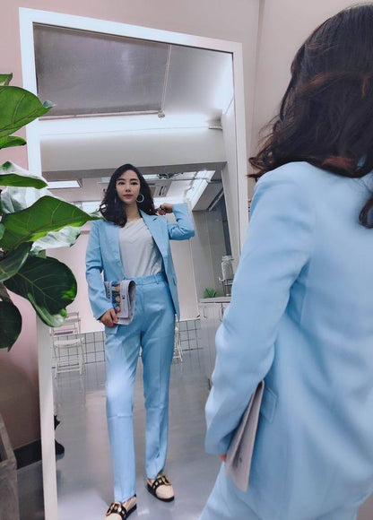 Woman in light blue suit posing confidently in front of mirror at FashionRay store