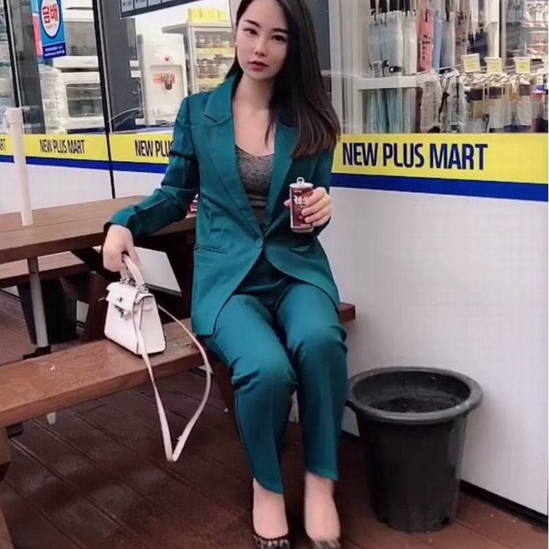 Woman in teal suit with white handbag sitting outside New Plus Mart, stylish fashion look
