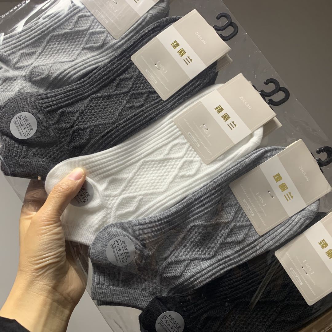 Hand holding packaged pairs of textured gray, white, and black socks, FashionRay comfort style