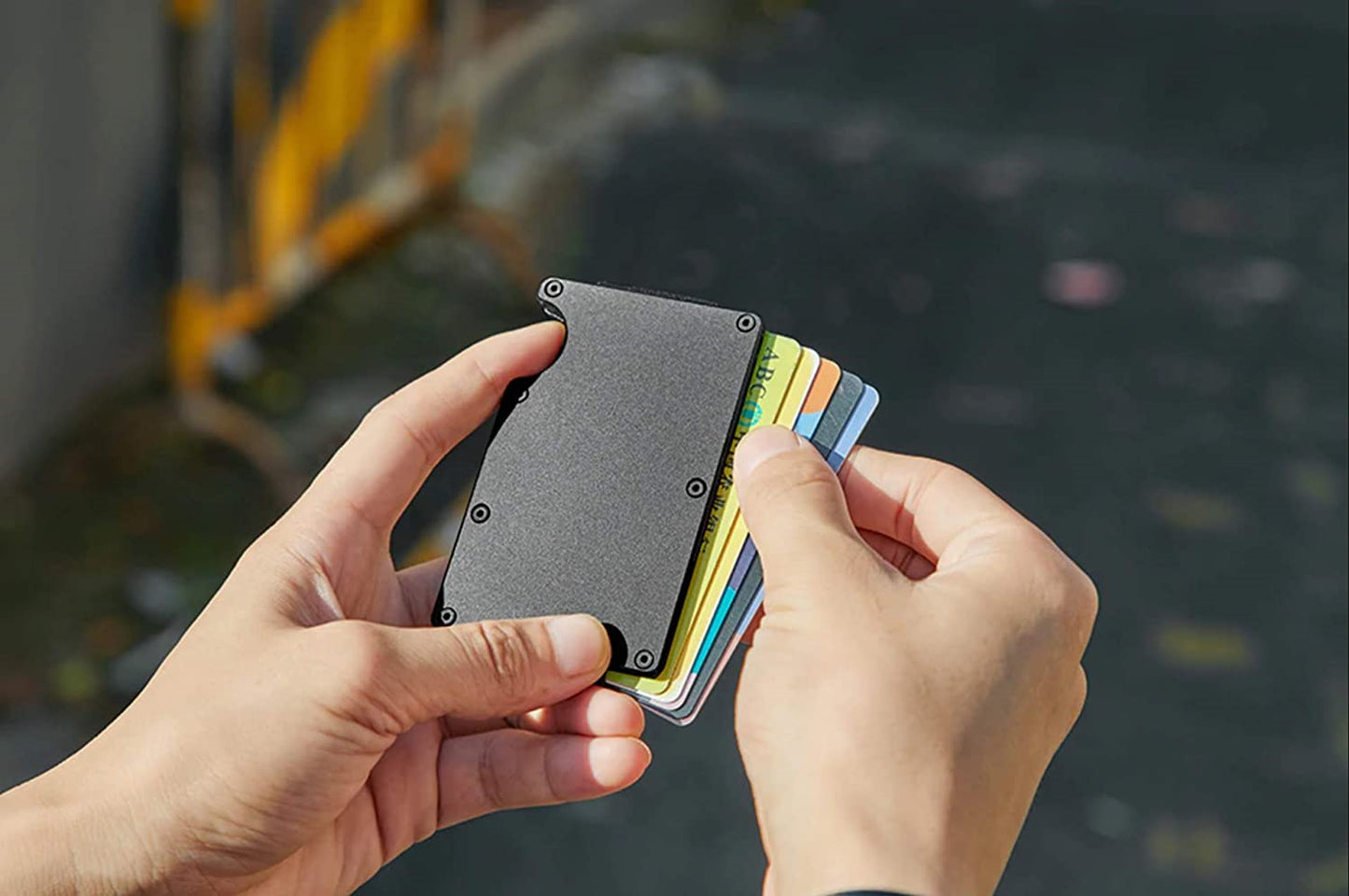 Hand holding slim black RFID card holder wallet with colorful cards outdoors, FashionRay style