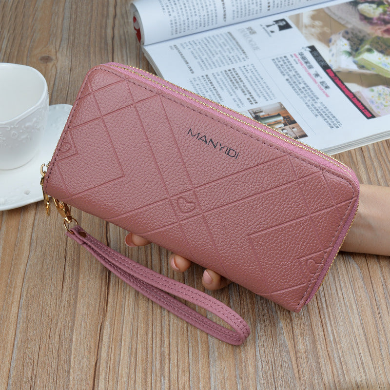 Pink textured wristlet wallet with gold zipper, held on wooden table, magazine and teacup nearby