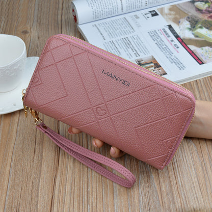 Pink textured wristlet wallet with gold zipper, held on wooden table, magazine and teacup nearby