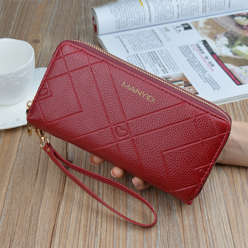 Red textured wristlet wallet with geometric patterns, held by hand on wooden table, FashionRay