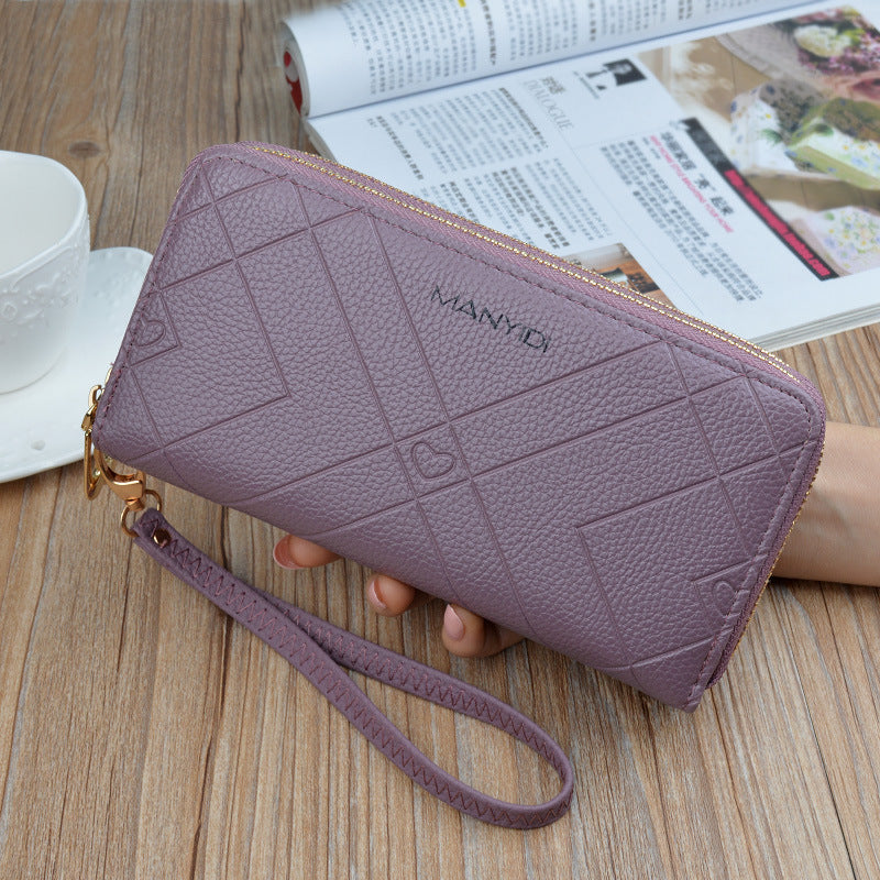 Purple textured wristlet wallet with geometric pattern, held on wood table near magazine.