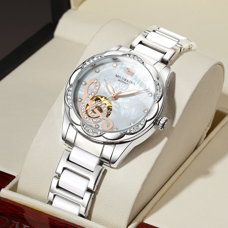 Elegant silver MG.ORIKINA women’s wristwatch with crystal accents on a white pillow, FashionRay.