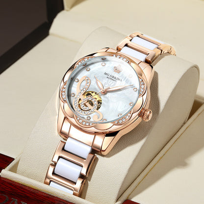 Rose gold luxury women’s watch with crystal accents on white strap, displayed in case