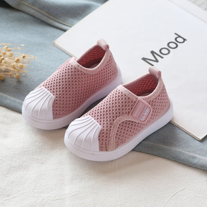 Pink mesh slip-on kids sneakers with white rubber toe caps, displayed on light fabric