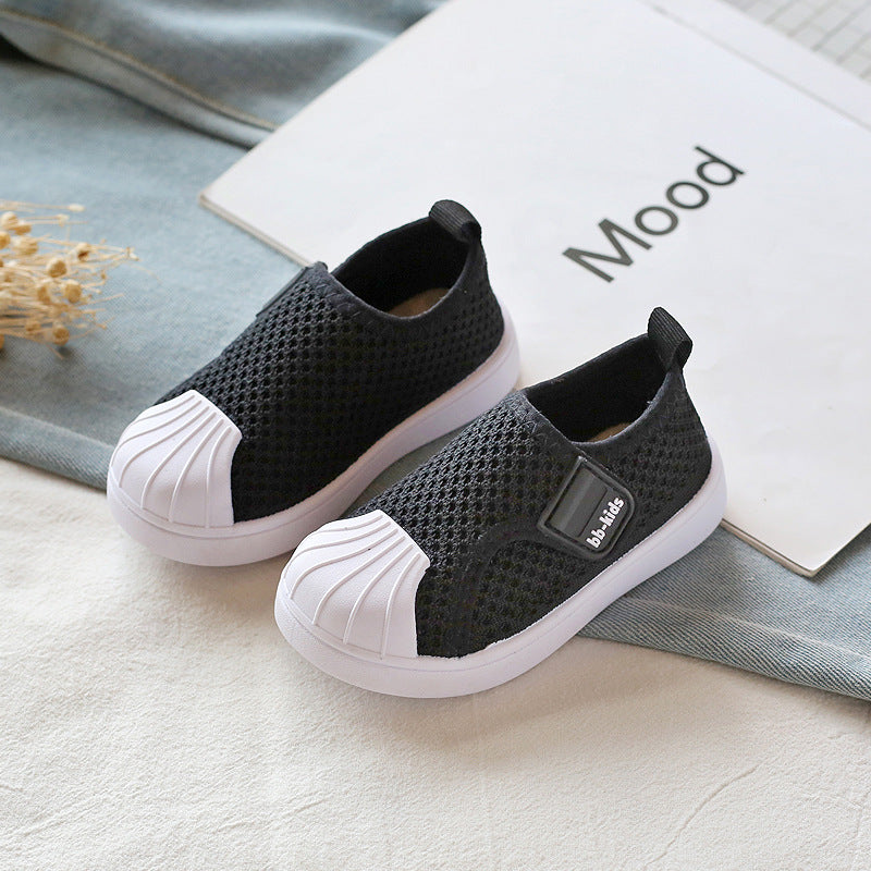 Black mesh slip-on kids sneakers with white rubber toe caps on neutral background, FashionRay