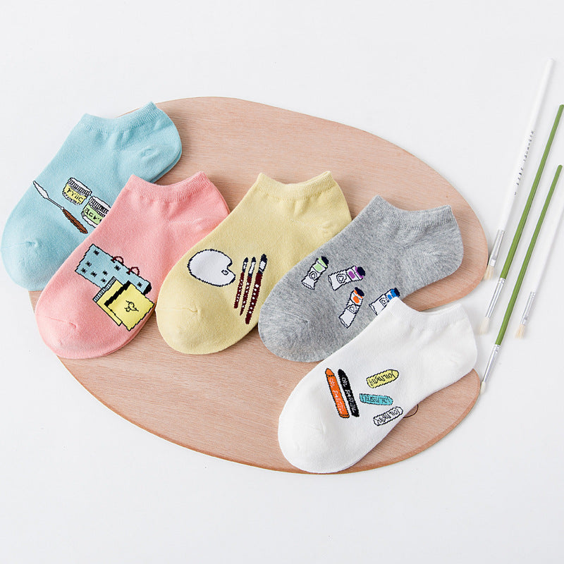 Colorful ankle socks with cute art supply designs, displayed on a wooden tray, FashionRay.