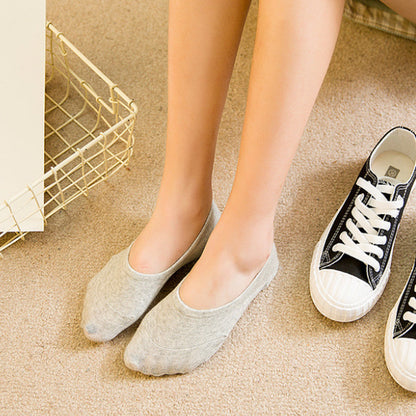 Woman wearing gray no-show socks sitting next to black sneakers on beige carpet, FashionRay