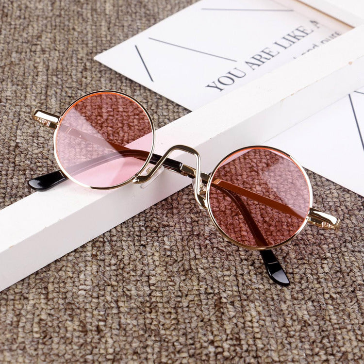 Round pink-lens sunglasses with gold frame on textured surface, FashionRay accessory