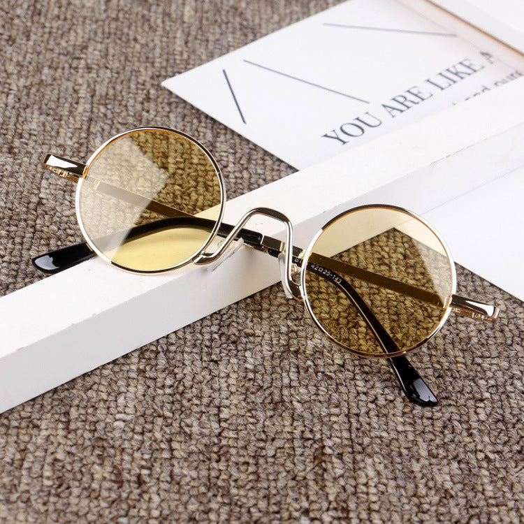 Round gold frame sunglasses with yellow lenses on a textured surface, FashionRay style