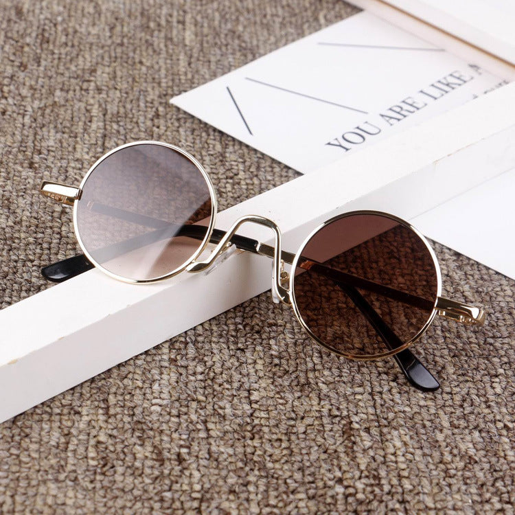 Round gold frame sunglasses with brown lenses on a textured surface, FashionRay style