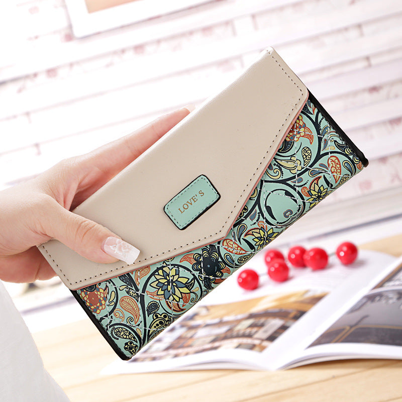 Hand holding a FashionRay floral wallet with beige flap and colorful print, on a wooden table