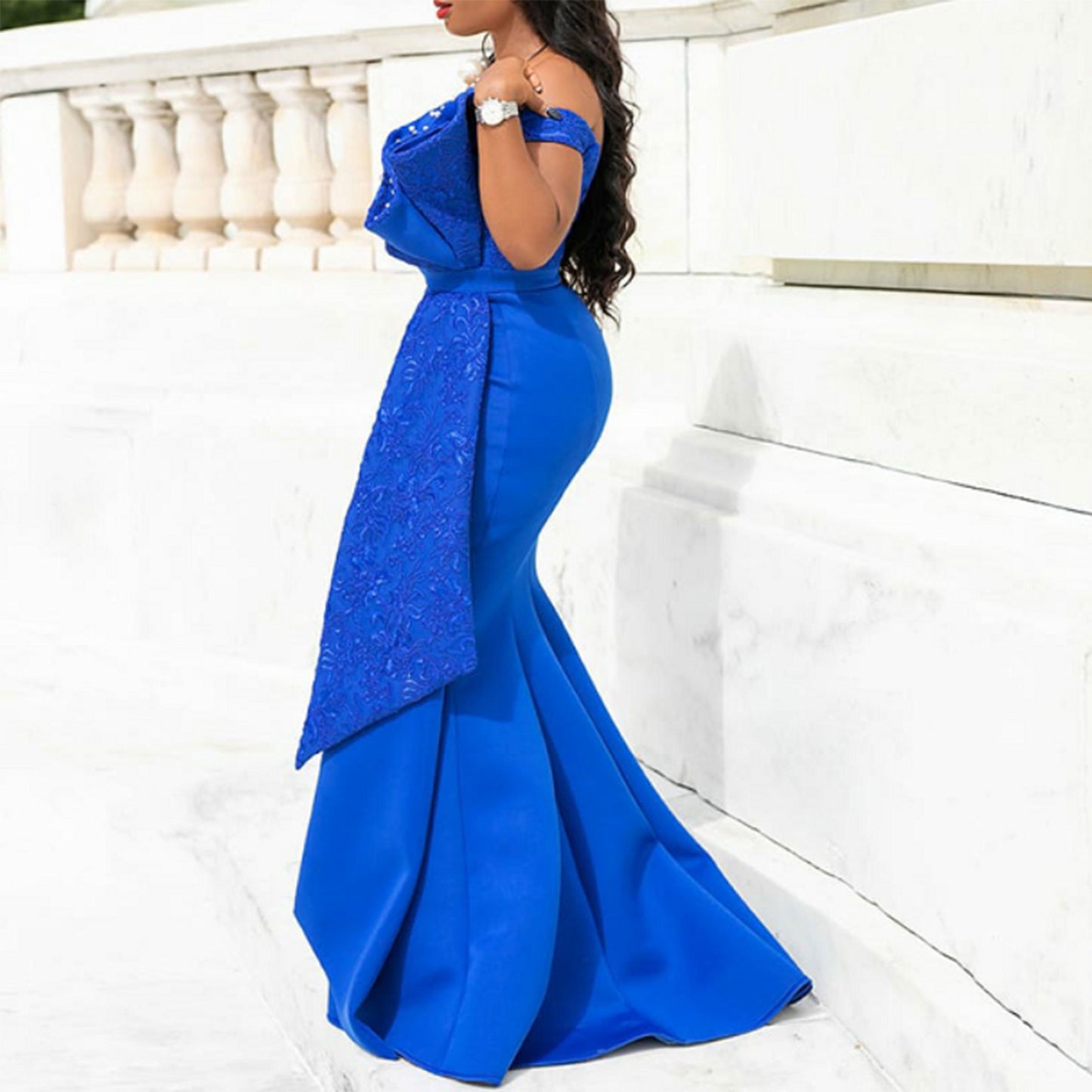 Woman in elegant royal blue off-shoulder gown with lace details, posing outdoors
