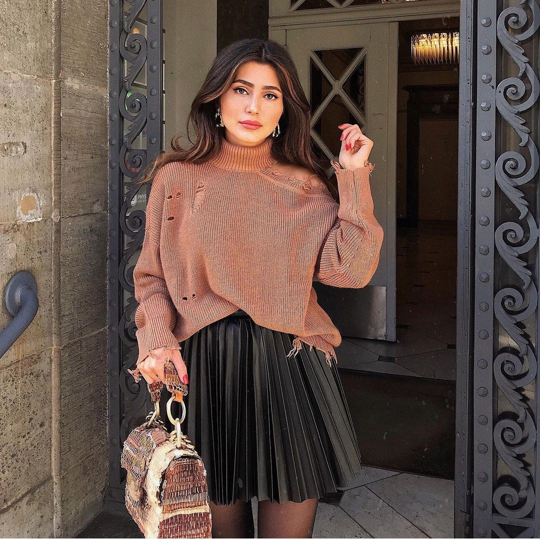 Woman in a brown distressed sweater and black pleated skirt holding a textured bag, FashionRay style