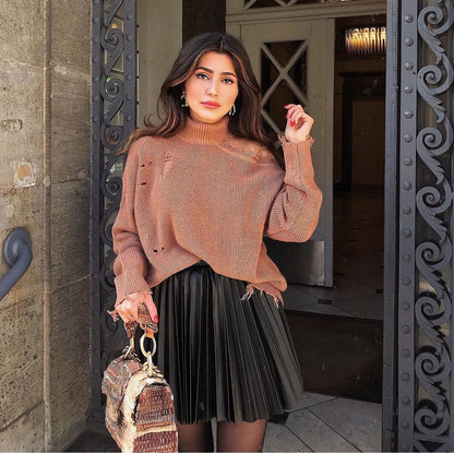 Woman in a brown distressed sweater and black pleated skirt holding a textured bag, FashionRay style