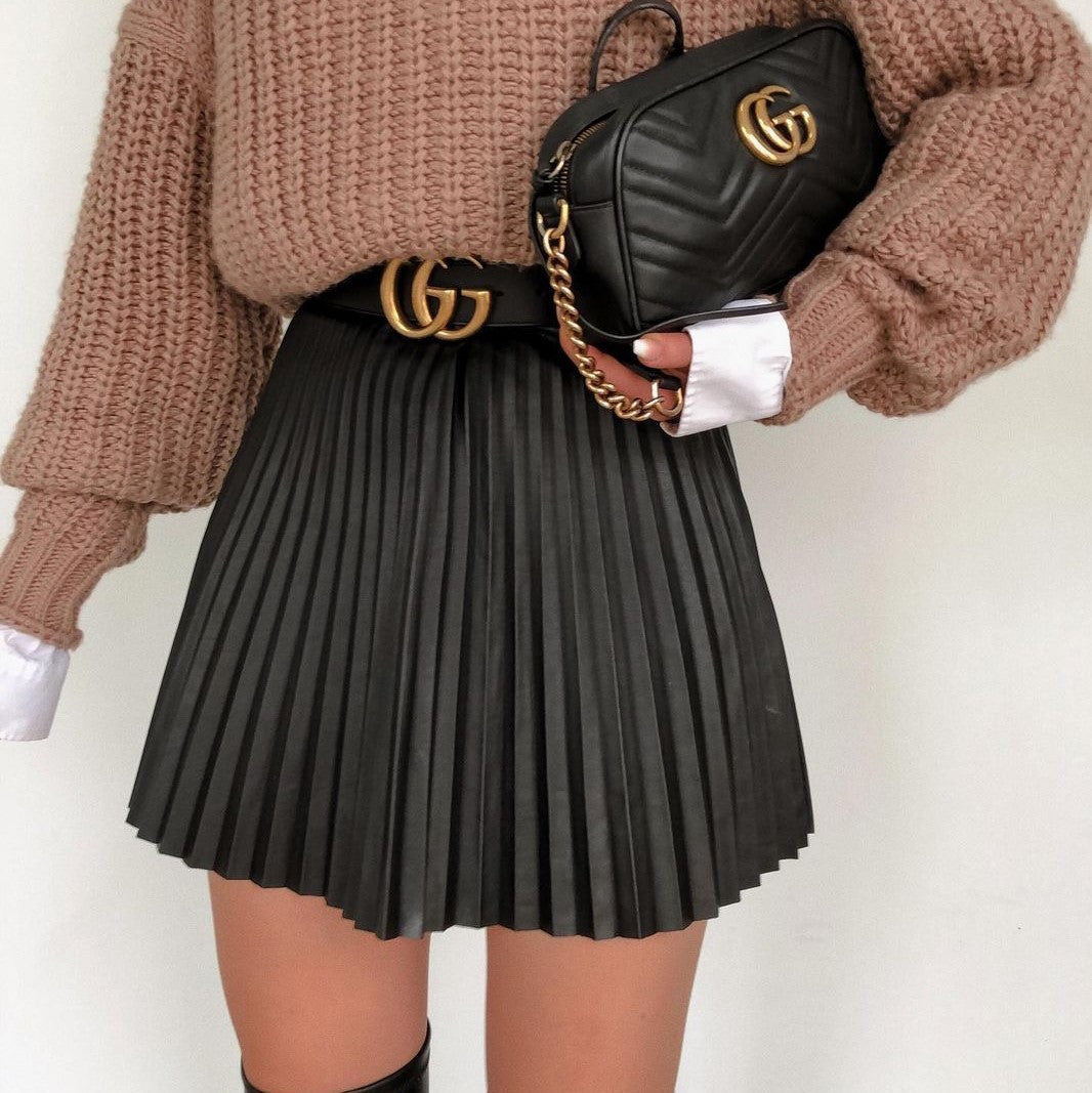 Woman wearing chunky knit sweater, black pleated skirt, and chic handbag, FashionRay style