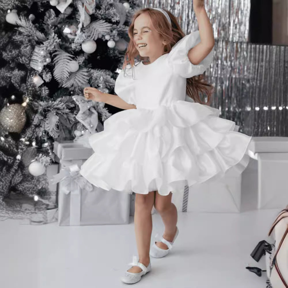 Smiling girl in ruffled white dress dancing by a silver Christmas tree with gifts, FashionRay