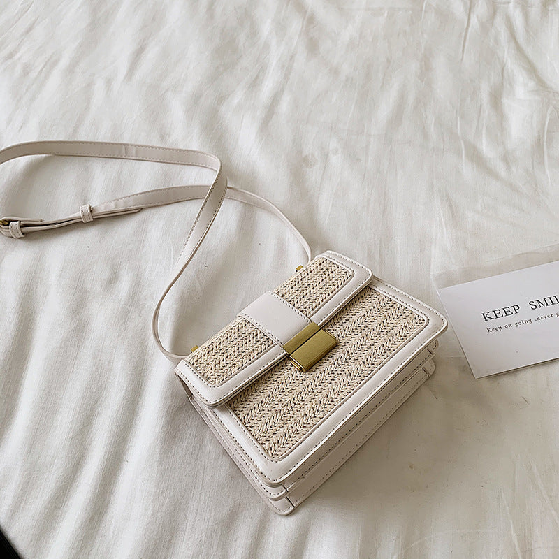Trendy woven crossbody bag with white leather trim and gold clasp on white bedding