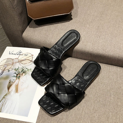 Black woven leather slide sandals on a beige couch with a brown bag, FashionRay style