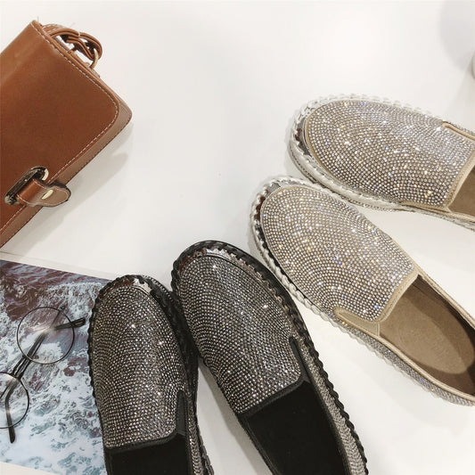 Sparkly slip-on loafers in gold and black with a brown purse, stylish eyewear on white table