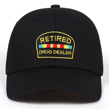 Black cap with yellow embroidered patch reading 'Retired Drug Dealer,' colorful stripes