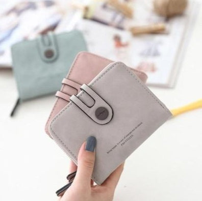 Hand holding a pastel gray wallet in front of styled pink and green wallets, FashionRay accessories