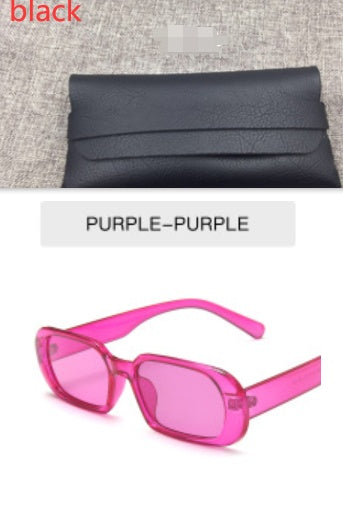 Black textured clutch purse on fabric and purple-pink sunglasses, FashionRay accessories.