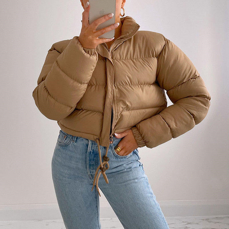 Woman wearing light brown puffer jacket and blue jeans, taking mirror selfie, FashionRay style