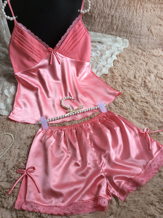 Pink satin camisole and shorts sleepwear set with lace trim on soft beige surface