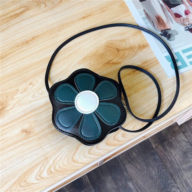 Flower-shaped black crossbody bag with green petals on wooden table, stylish accessory at FashionRay