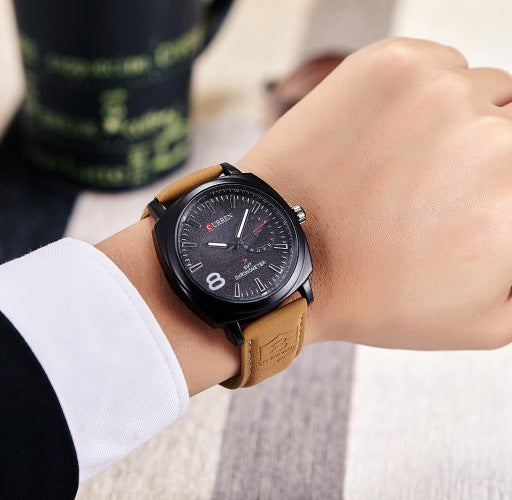 Stylish black watch with tan leather strap on wrist, modern accessory at FashionRay