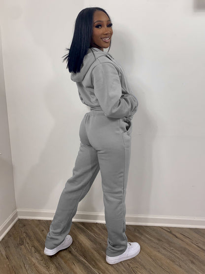 Woman modeling a light gray hoodie and sweatpants set with white sneakers on wood floor, FashionRay style