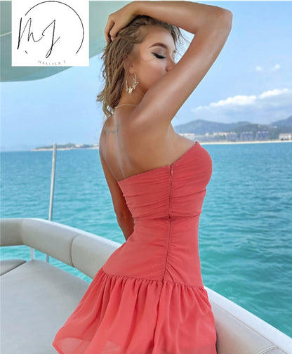 Woman in coral strapless dress posing on a yacht, ocean and mountains in background, FashionRay style.