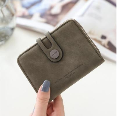 Hand holding a minimalist olive green wallet with clasp in a stylish, modern setting